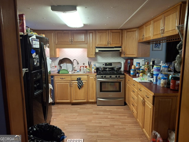 kitchen with gas range, light wood-type flooring, under cabinet range hood, a sink, and black fridge