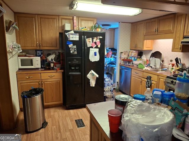 kitchen with brown cabinets, appliances with stainless steel finishes, a sink, light wood-style floors, and wallpapered walls