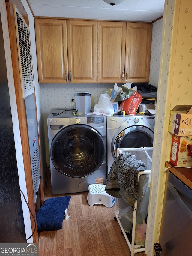 clothes washing area with cabinet space, a heating unit, wallpapered walls, wood finished floors, and washing machine and dryer