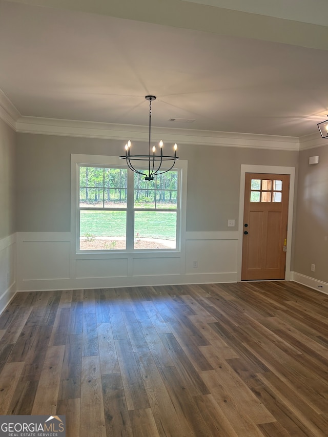 unfurnished dining area featuring a notable chandelier, ornamental molding, and dark wood-type flooring