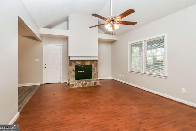 unfurnished living room featuring vaulted ceiling, ceiling fan, dark wood-type flooring, and a stone fireplace