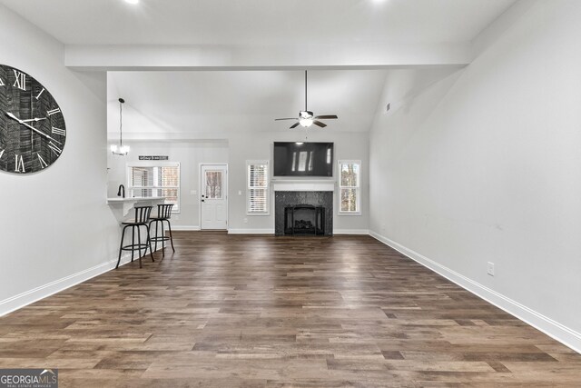 unfurnished living room featuring ceiling fan with notable chandelier, dark wood-type flooring, a high end fireplace, and vaulted ceiling