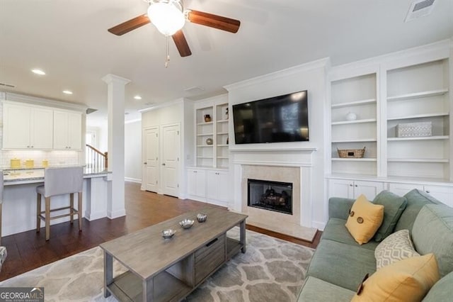 living room with built in shelves, ceiling fan, and dark wood-type flooring