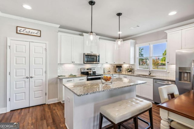 kitchen featuring appliances with stainless steel finishes, sink, pendant lighting, white cabinets, and a center island