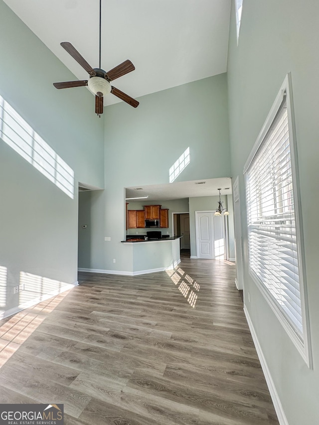 unfurnished living room featuring ceiling fan, wood-type flooring, and a towering ceiling