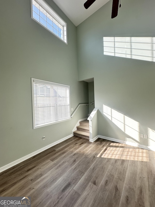 unfurnished living room featuring a towering ceiling, light hardwood / wood-style flooring, and ceiling fan