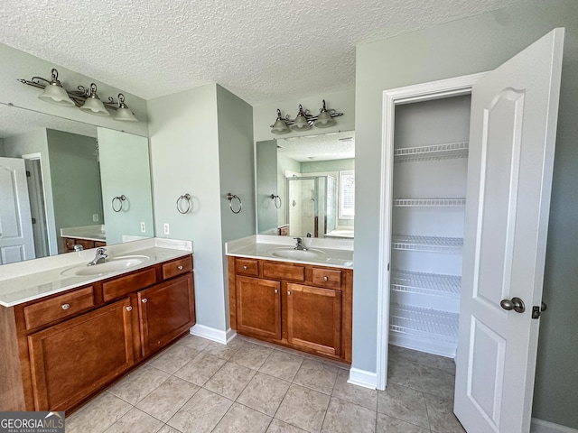 bathroom with tile patterned flooring, vanity, a shower with door, and a textured ceiling