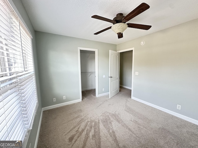 unfurnished bedroom with a closet, a walk in closet, light colored carpet, and ceiling fan