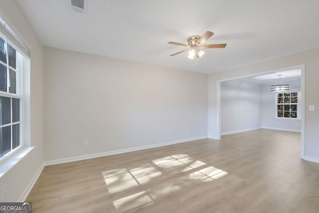 unfurnished room featuring ceiling fan with notable chandelier and light wood-type flooring