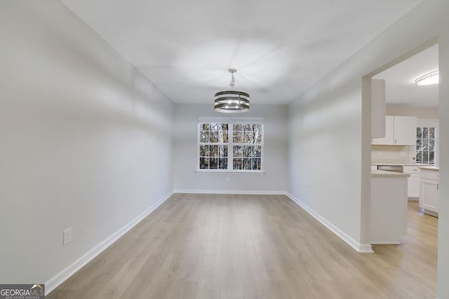 unfurnished dining area featuring a notable chandelier, plenty of natural light, and light hardwood / wood-style floors