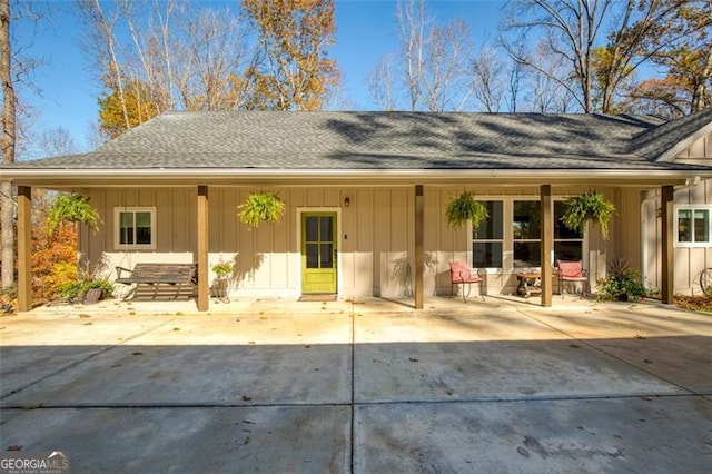 rear view of house featuring board and batten siding, a patio area, and a shingled roof