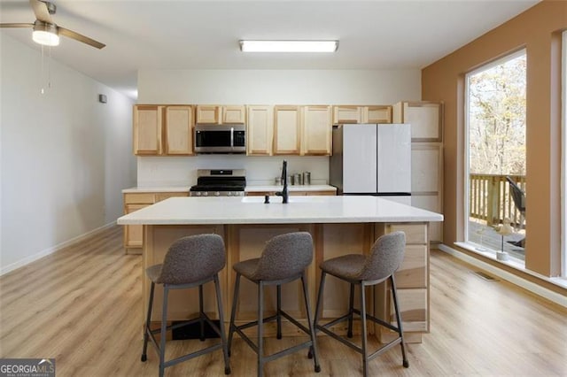 kitchen with an island with sink, light brown cabinetry, light wood-style flooring, light countertops, and appliances with stainless steel finishes