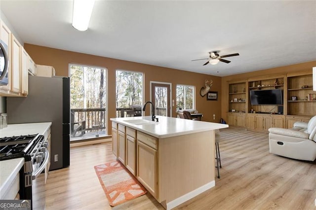 kitchen featuring light wood-style flooring, a sink, open floor plan, a ceiling fan, and stainless steel gas range oven