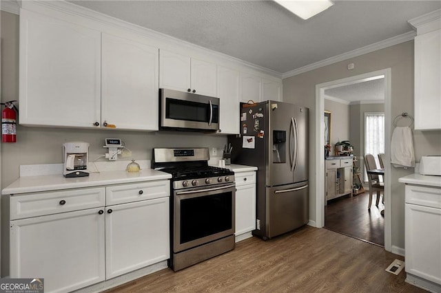 kitchen featuring dark wood-type flooring, ornamental molding, appliances with stainless steel finishes, white cabinets, and light countertops