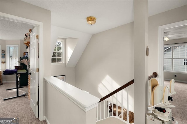 hall featuring carpet flooring, an upstairs landing, baseboards, and a textured ceiling