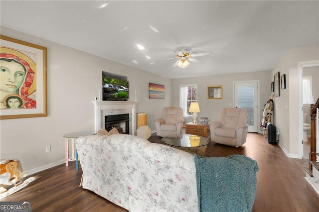 living area featuring baseboards, dark wood-type flooring, a ceiling fan, and a premium fireplace