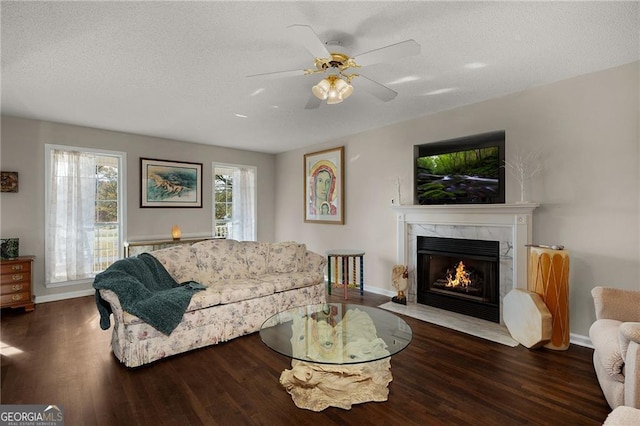 living room featuring baseboards, a premium fireplace, wood finished floors, a textured ceiling, and a ceiling fan