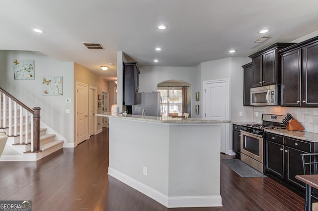 kitchen with backsplash, light stone countertops, dark hardwood / wood-style flooring, and stainless steel appliances