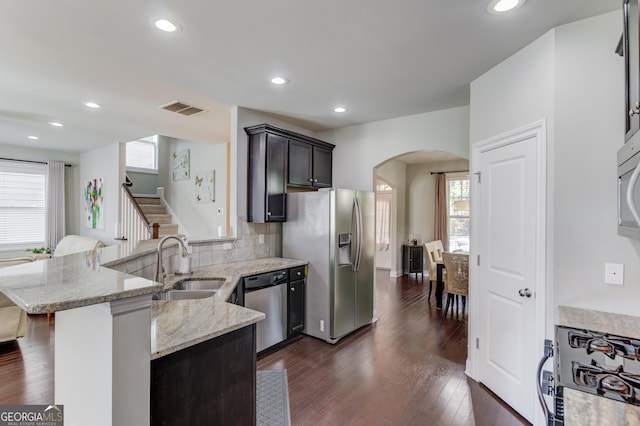 kitchen featuring sink, dark hardwood / wood-style floors, decorative backsplash, appliances with stainless steel finishes, and light stone counters