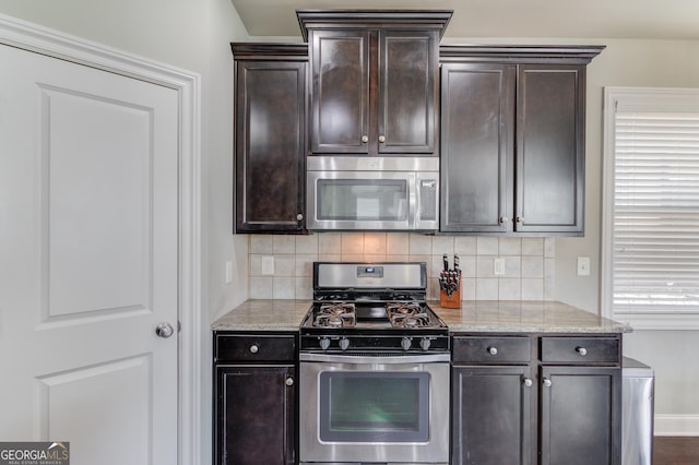 kitchen with dark brown cabinetry, decorative backsplash, light stone countertops, and appliances with stainless steel finishes