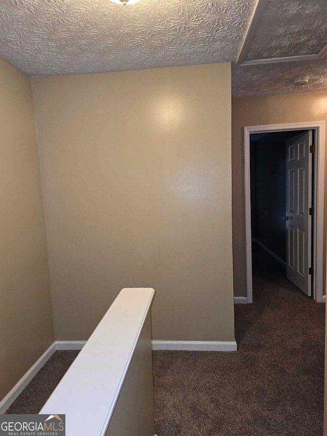 corridor with a textured ceiling and dark colored carpet