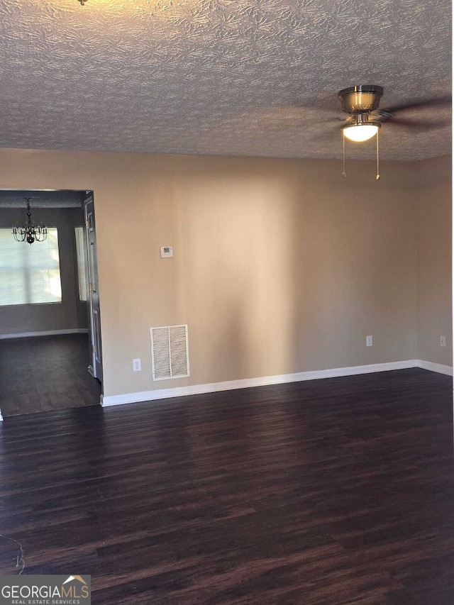 empty room featuring a chandelier, a textured ceiling, and dark wood-type flooring