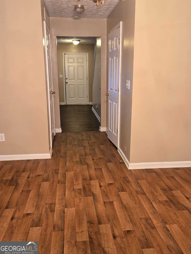 corridor with a textured ceiling and dark wood-type flooring