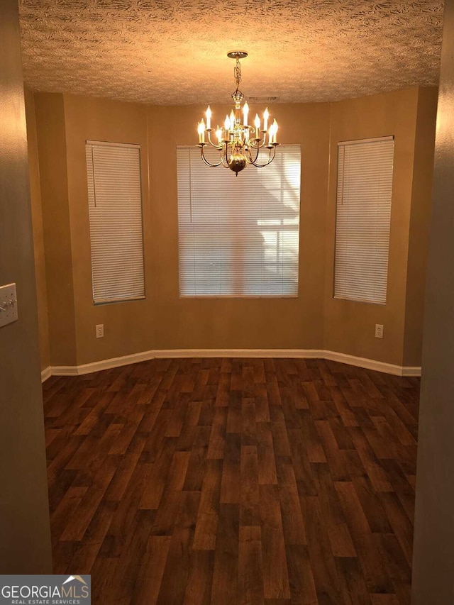 unfurnished room with dark hardwood / wood-style flooring, a chandelier, and a textured ceiling