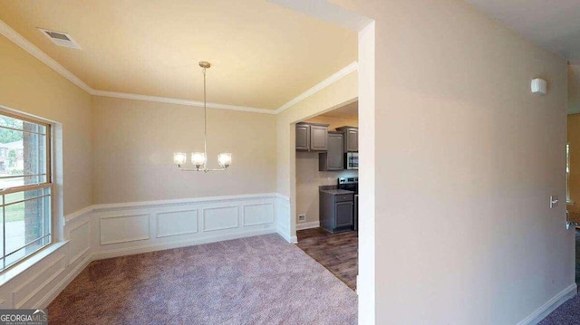 unfurnished dining area featuring crown molding, a notable chandelier, and dark colored carpet