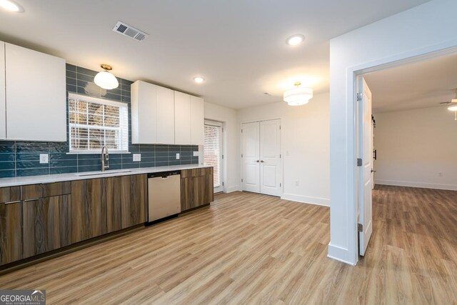 kitchen featuring sink, stainless steel dishwasher, tasteful backsplash, light hardwood / wood-style floors, and white cabinetry