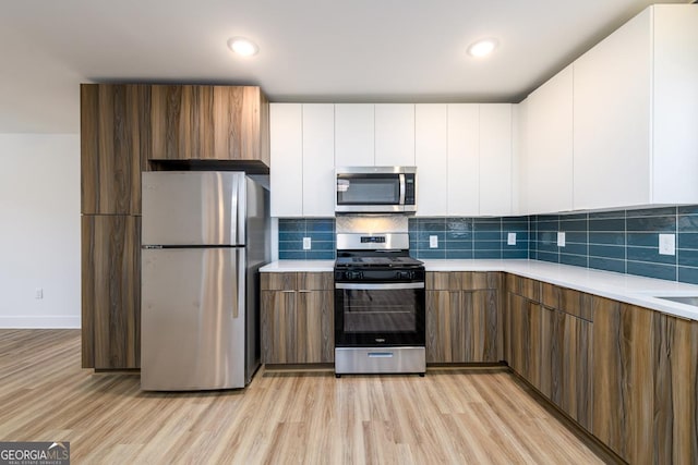 kitchen with appliances with stainless steel finishes, light wood-type flooring, white cabinetry, and backsplash