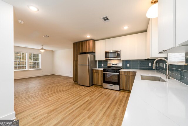 kitchen featuring appliances with stainless steel finishes, ceiling fan, sink, light hardwood / wood-style flooring, and white cabinets