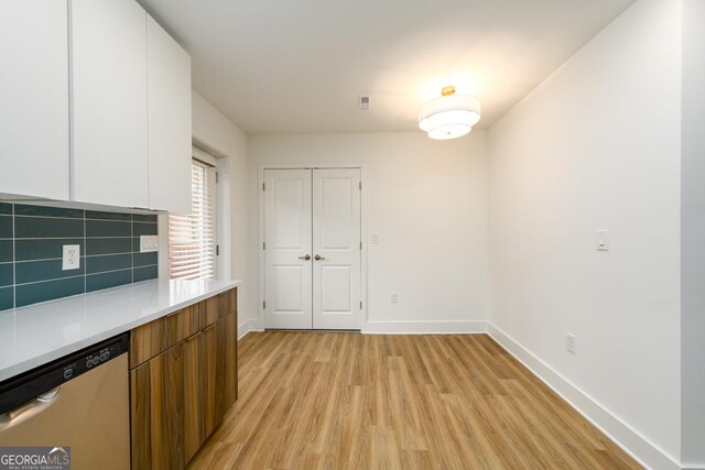 kitchen with backsplash, white cabinetry, stainless steel dishwasher, and light hardwood / wood-style floors