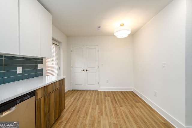 kitchen featuring white cabinetry, decorative backsplash, stainless steel dishwasher, and light wood-type flooring