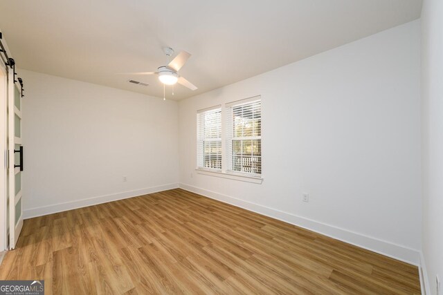 unfurnished room with a barn door, light hardwood / wood-style flooring, and ceiling fan