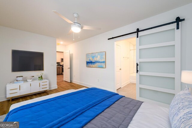 bedroom featuring light wood-type flooring, a barn door, ensuite bathroom, and ceiling fan