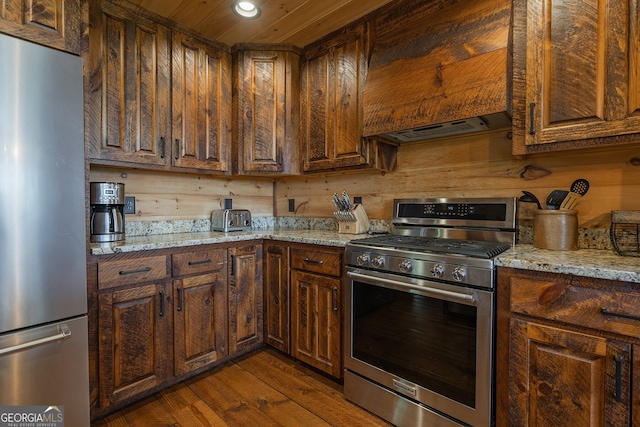 kitchen featuring light stone countertops, dark hardwood / wood-style flooring, stainless steel appliances, extractor fan, and wood walls