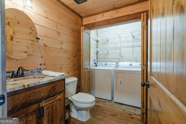 bathroom featuring washing machine and dryer, wooden walls, toilet, and hardwood / wood-style flooring