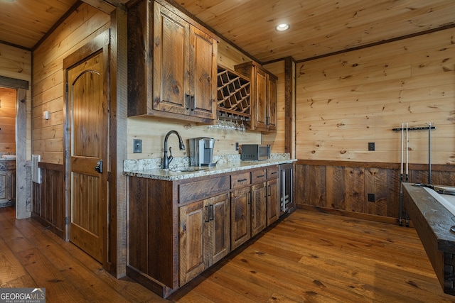 kitchen with wood walls, sink, light stone counters, and dark hardwood / wood-style floors