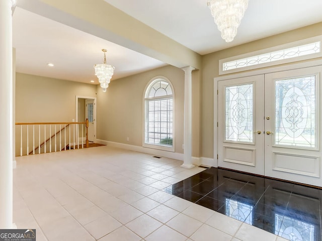 foyer entrance with french doors, decorative columns, an inviting chandelier, and tile patterned floors