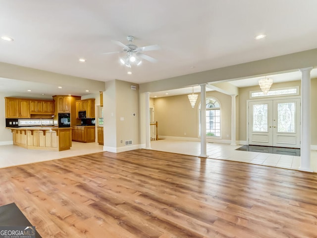 unfurnished living room with french doors, ceiling fan with notable chandelier, and light wood-type flooring