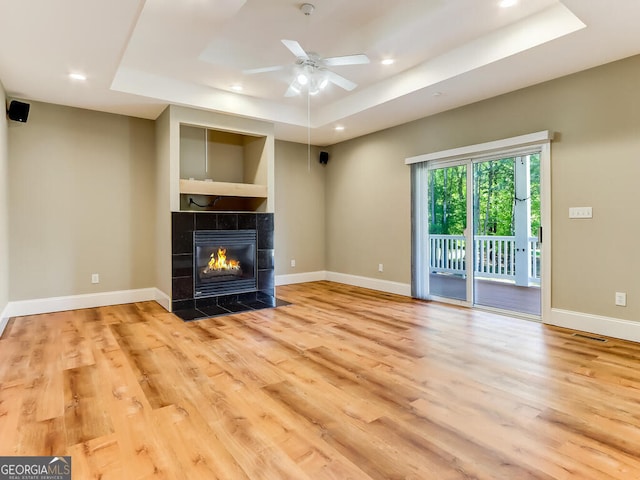 unfurnished living room featuring ceiling fan, light wood-type flooring, and a tray ceiling