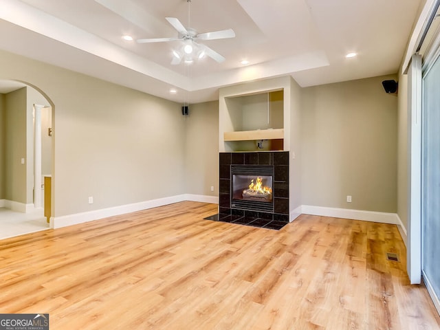 unfurnished living room with a tray ceiling, a tile fireplace, ceiling fan, and light hardwood / wood-style floors