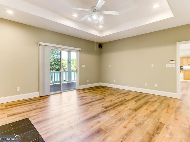 empty room with a tray ceiling, light hardwood / wood-style flooring, and ceiling fan