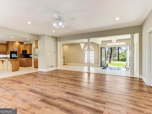 unfurnished living room featuring ceiling fan with notable chandelier, light hardwood / wood-style floors, and decorative columns