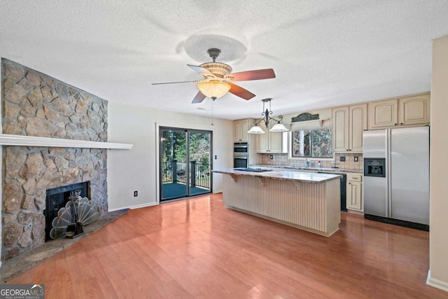 kitchen with appliances with stainless steel finishes, tasteful backsplash, a fireplace, a center island, and light hardwood / wood-style floors