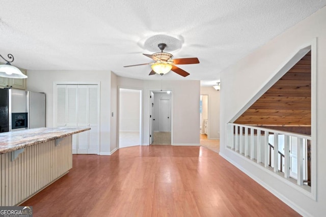 kitchen with pendant lighting, ceiling fan, stainless steel fridge, a textured ceiling, and light hardwood / wood-style floors