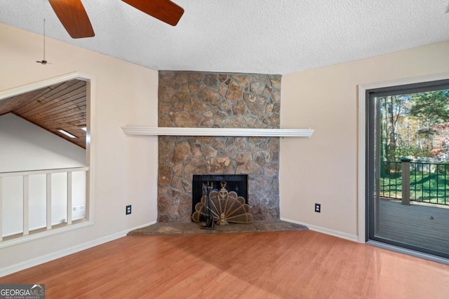 unfurnished living room featuring a stone fireplace, ceiling fan, hardwood / wood-style floors, and a textured ceiling