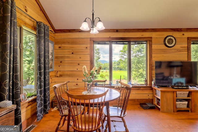 dining room featuring hardwood / wood-style floors, vaulted ceiling, wooden walls, and a chandelier