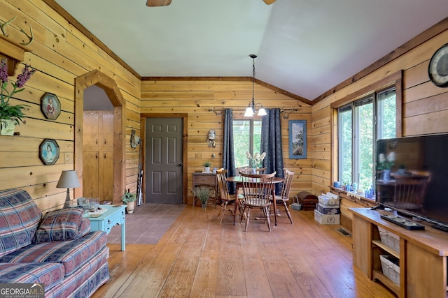 dining space with a chandelier, wooden walls, light hardwood / wood-style floors, and lofted ceiling